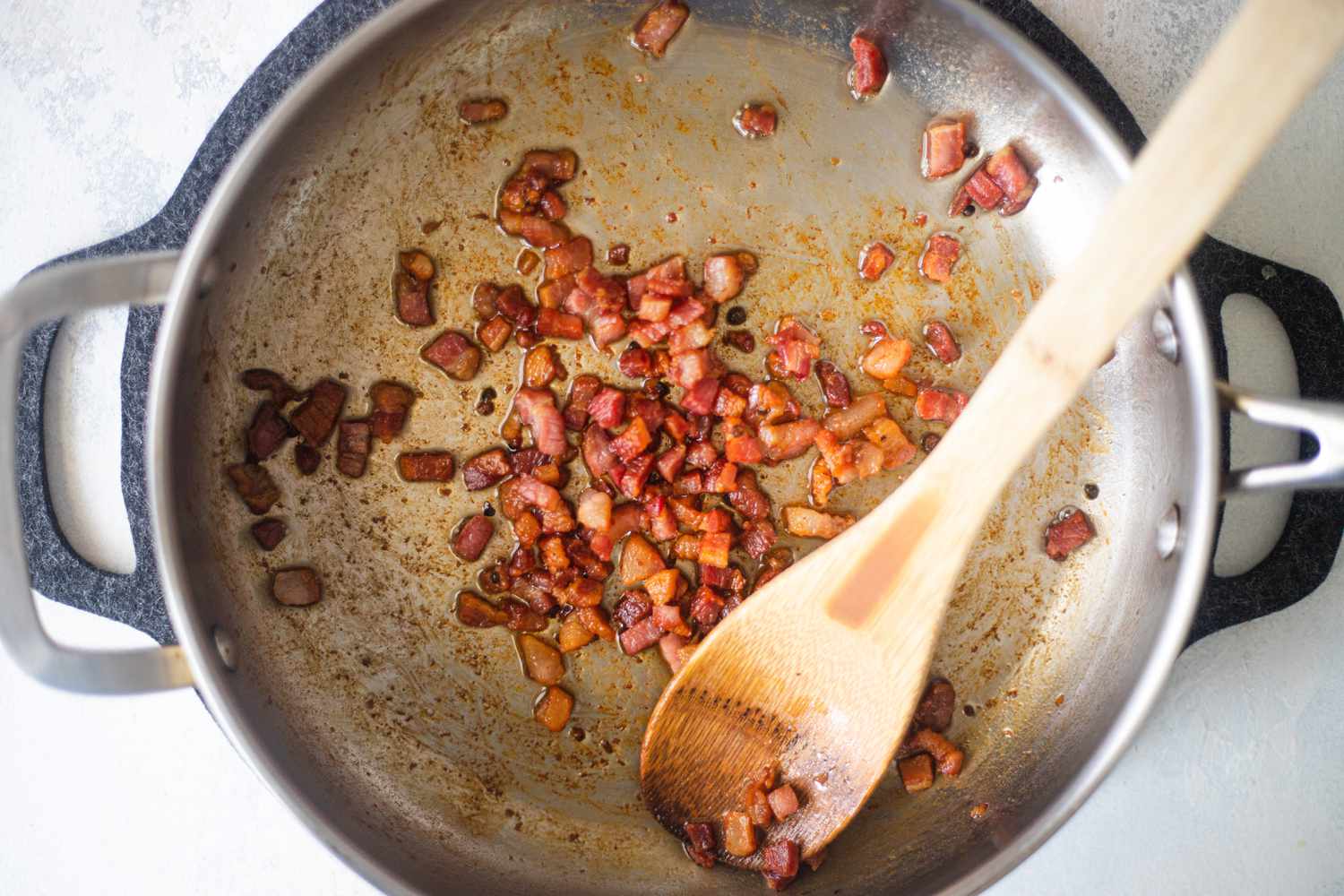 Top-down photo of diced bacon being browned in a sautÃ© pan