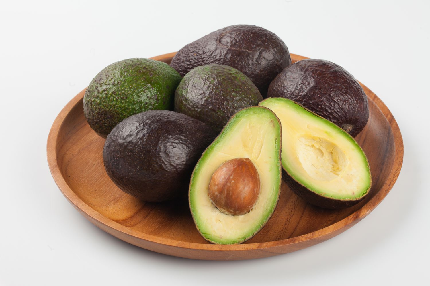 Several avocados on a wooden platter, with one avocado halved to show the pit