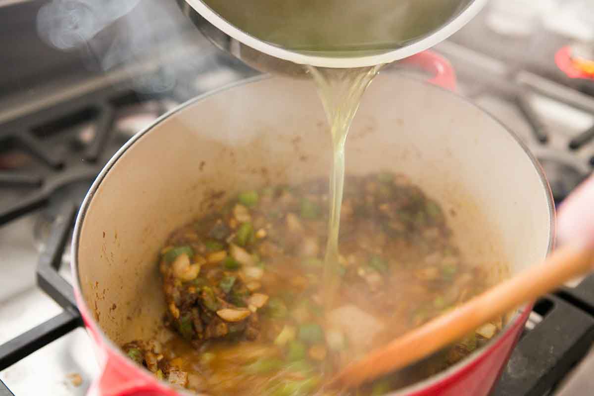 Slowly add the warm broth for the shrimp gumbo to the pot with the roux and vegetables