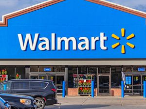 Exterior view of a Walmart store entrance with parked cars in the foreground