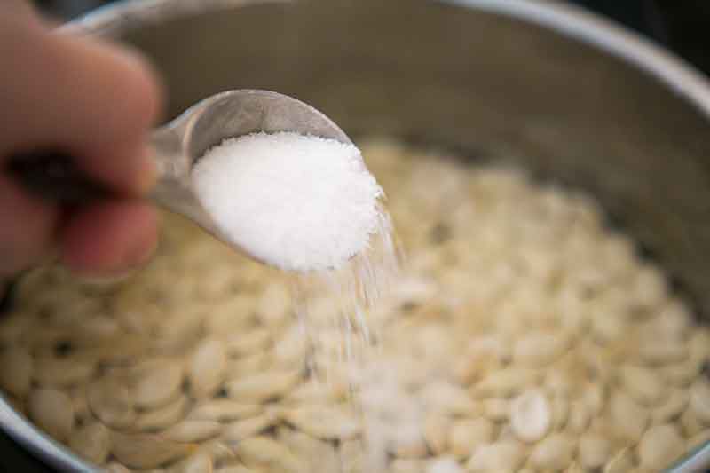 Salt being added to boiling pumpkin seeds before roasting