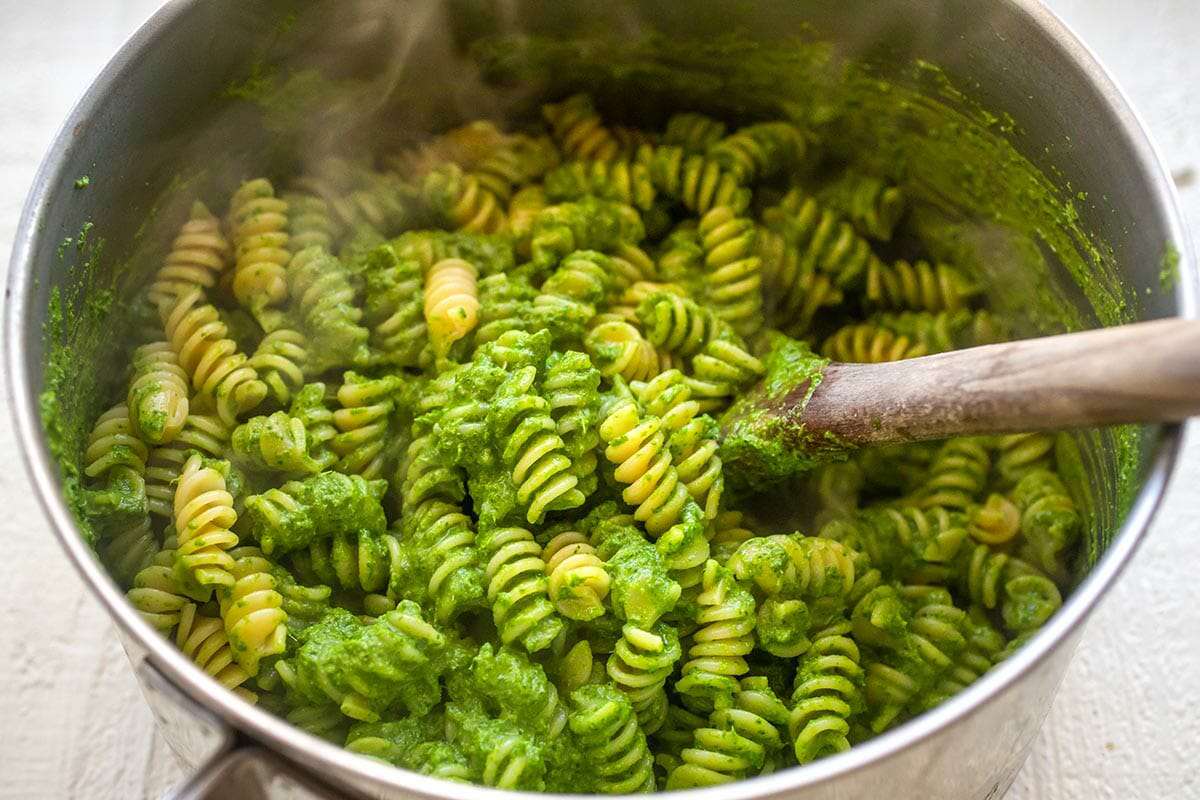Large stockpot of weeknight rotini and kale pesto being stirred together with a wooden spoon.