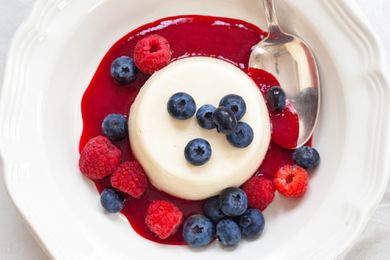 Panna Cotta with berries and sauce in a round bowl with a spoon.