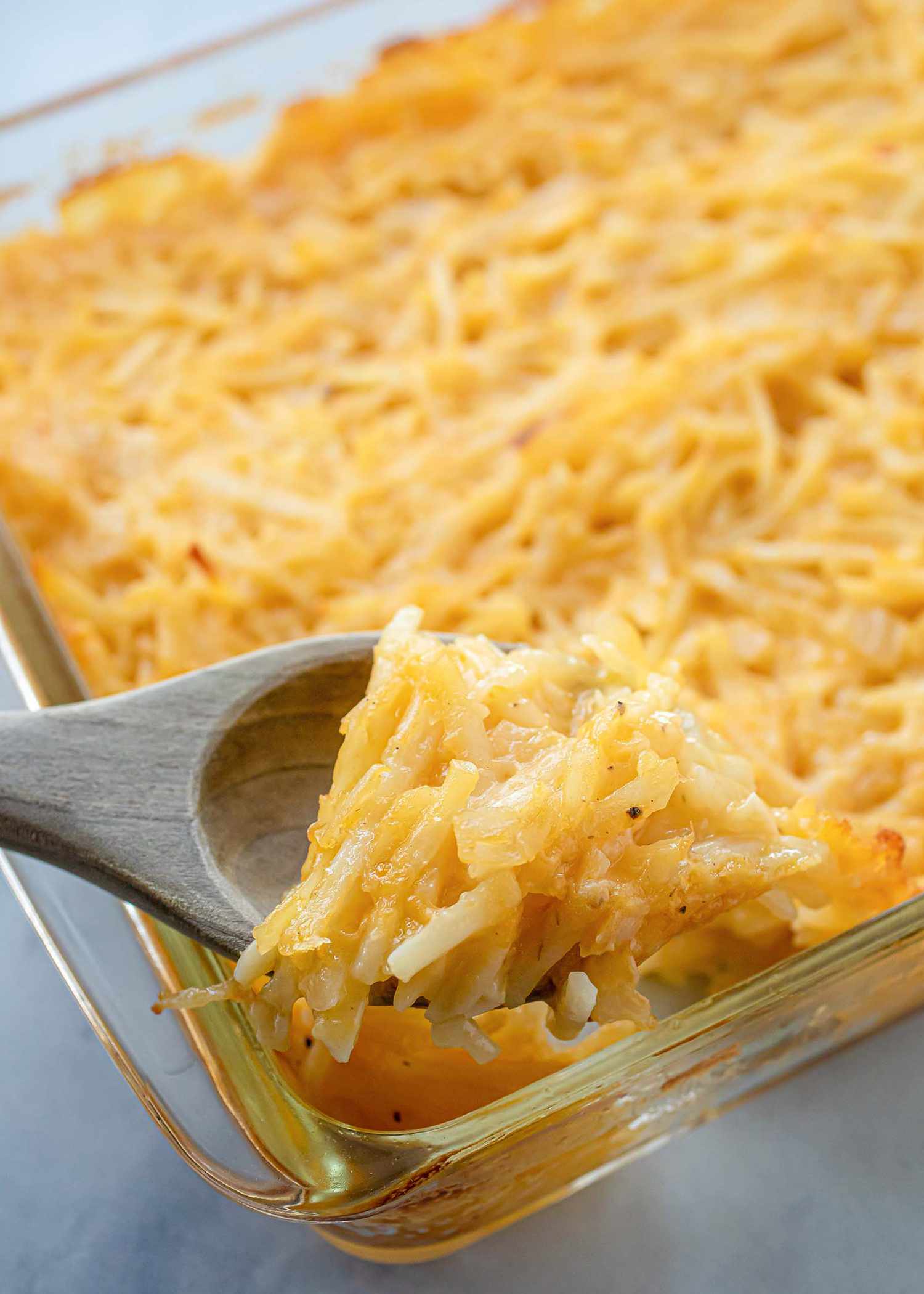 Close up view of a wooden spoon with a scoop of Mormon Funeral Potatoes being scooped out of a glass casserole dish.