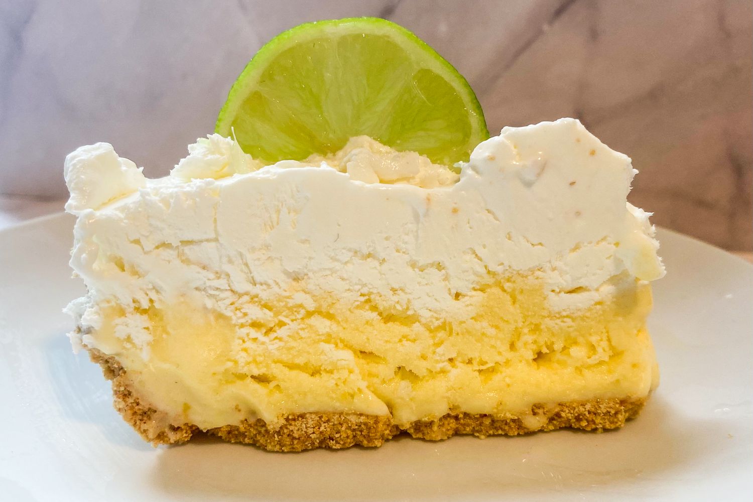 A slice of frozen key lime pie with a graham cracker crust and topped with a lime wedge