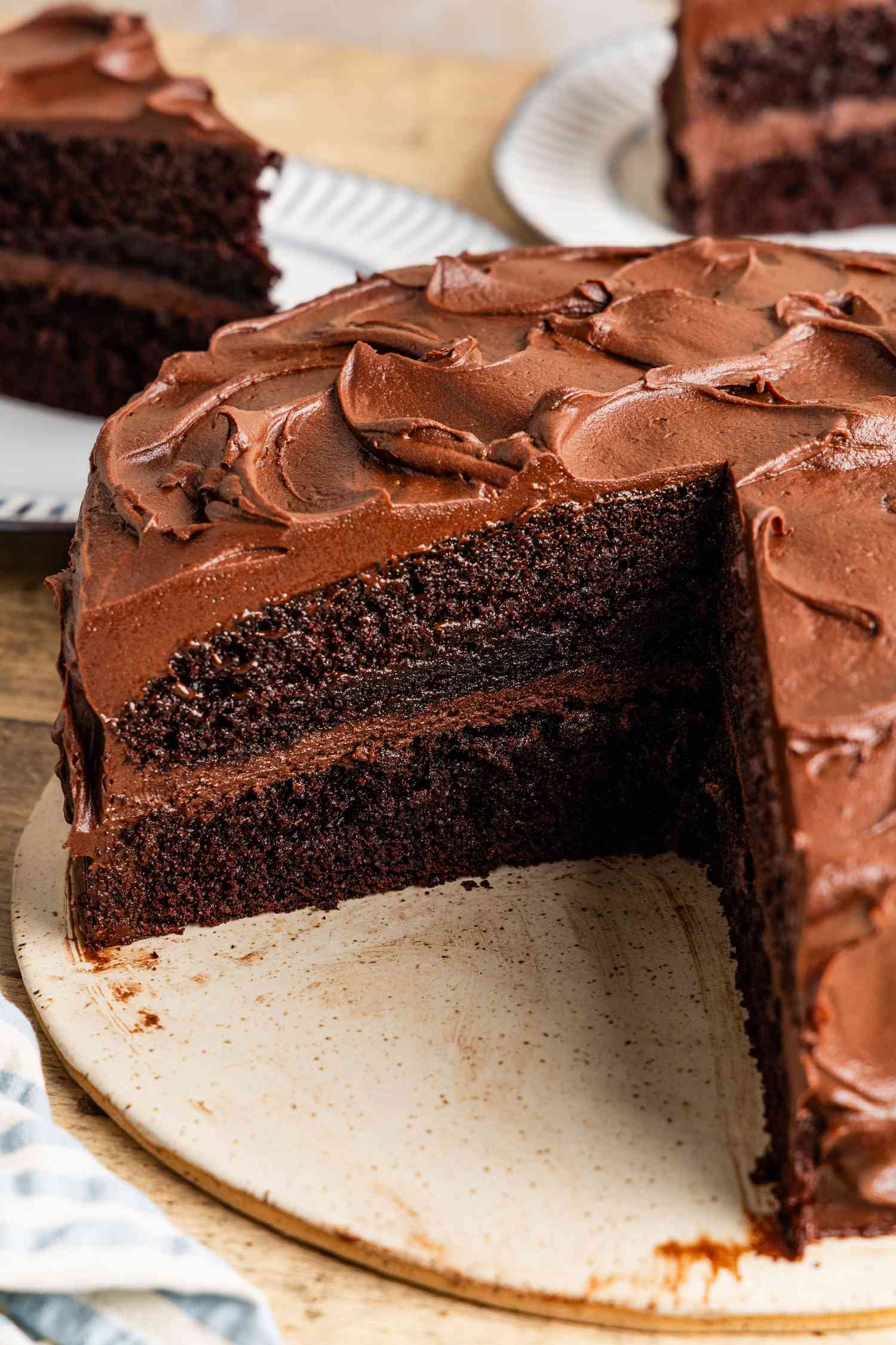 black magic cake on a platter with a slice cut out and in the background, two plates with some cake slices