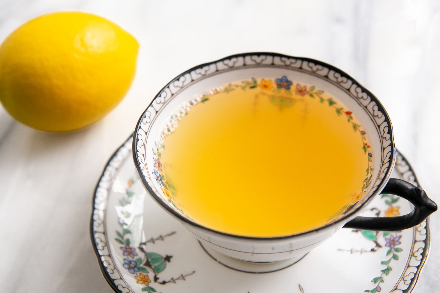 Teacup With Honey and Lemon Tea on a Saucer Next to a Lemon 