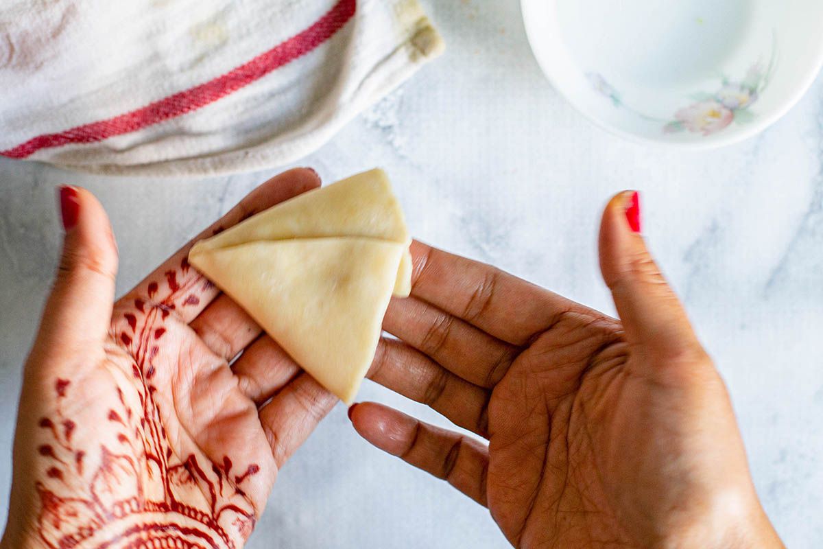 Woman with henna on her hands holding a cone of dough in her hands ot make Indian Samosas.