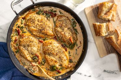 creamy tuscan chicken in a pot next to sliced bread on a wooden board and a glass of water 