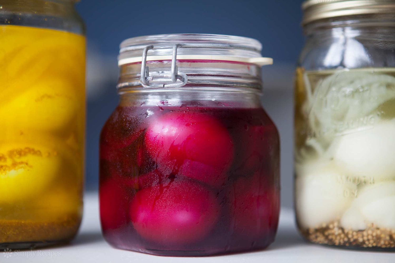 Three jars of pickled eggs; the middle jar includes pickle juice for bright pink eggs