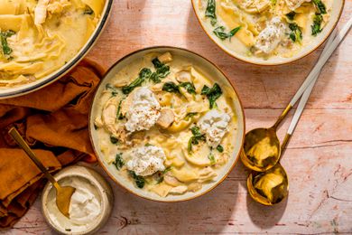 White chicken lasagna soup served in two bowls at a table setting with the spoons, napkins, and the rest of the soup in a dutch oven