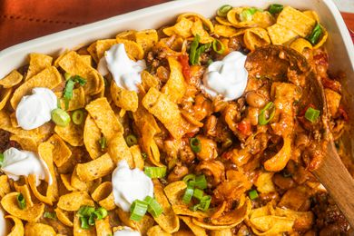 Walking taco casserole with dollops of sour cream in a casserole dish with a serving spoon (casserole dish missing some casserole)