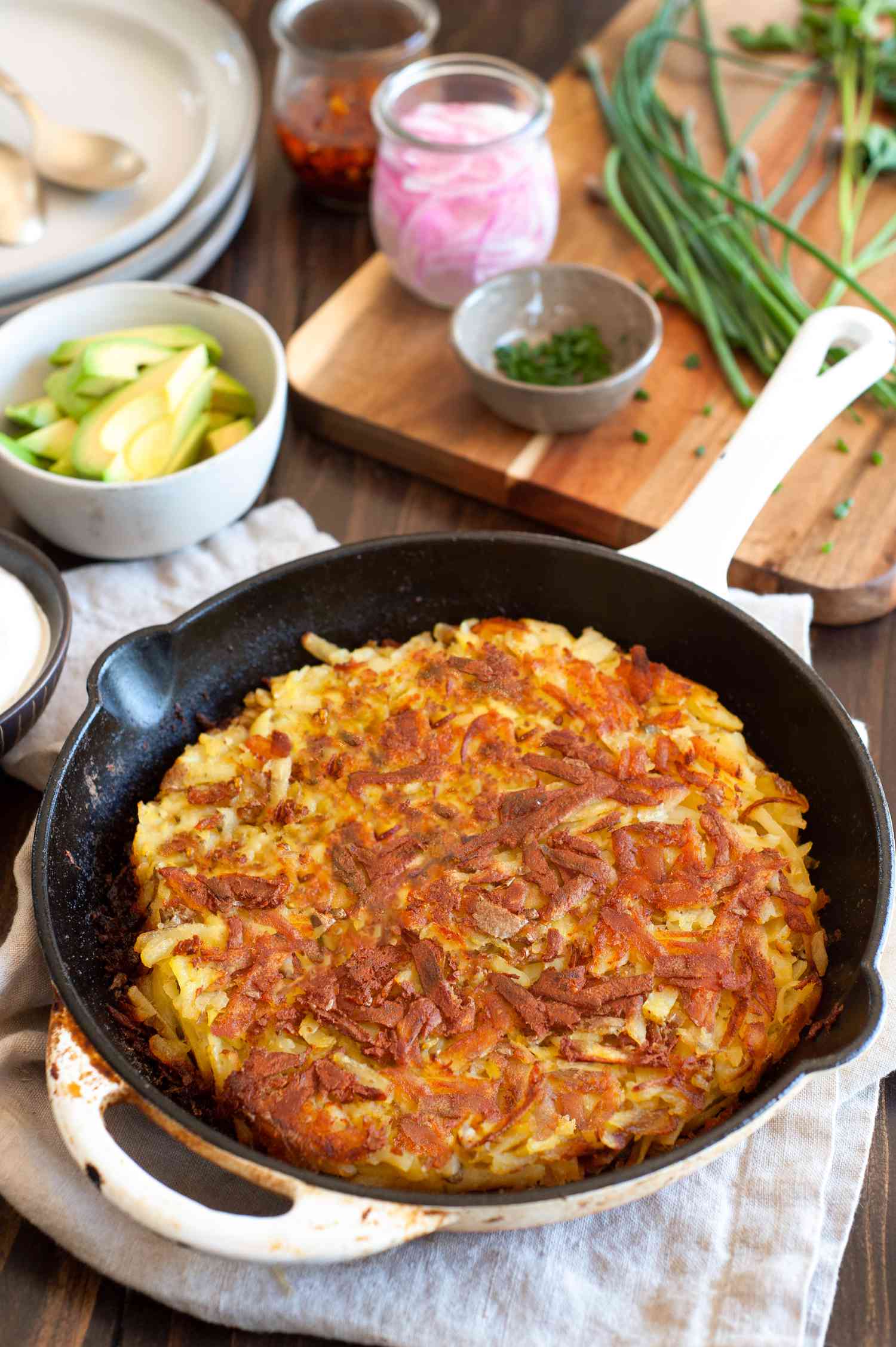 Rosti in a Skillet Surrounded by Bowls of Fixings (Avocado, Sour Cream, and Herbs)