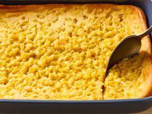 dark blue baking dish of corn soufflé with a spoon scooping out a serving