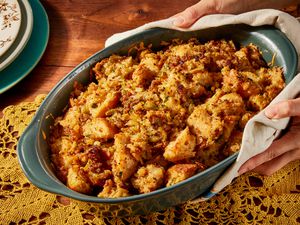 Two hands holding a green casserole dish of Wisconsin-style stuffing over a yellow doily on a wooden tabletop