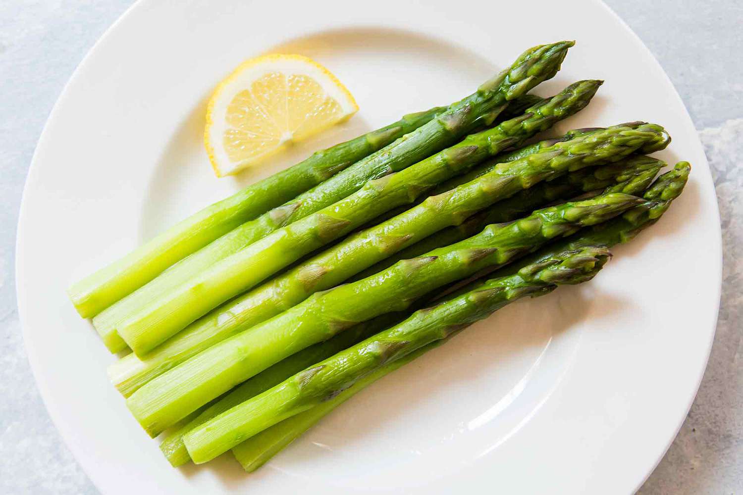 asparagus cooked on the stovetop on a white plate with a slice of lemon