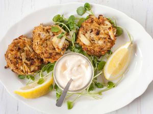 Maryland Crabcakes wtih greens and lemon wedges on a white plate wtih mayo