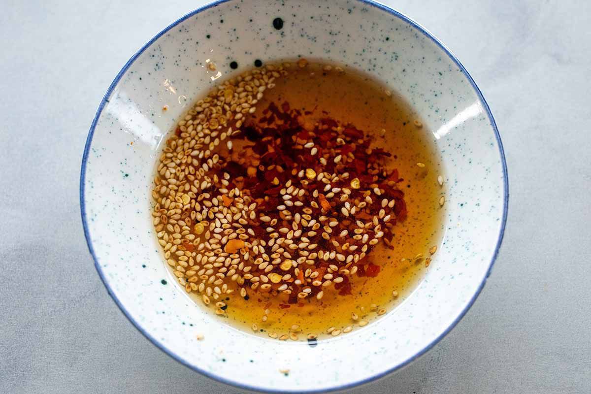 Blue speckled bowl with sesame seeds and sauce ingredients for Pork Fried Rice with Frozen Peas and Carrots.