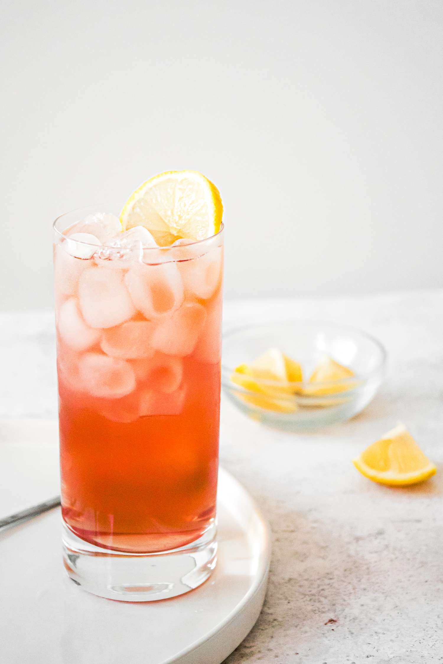 Sloe Gin Fizz with Ice and Lemon in Glass with Bowl of Lemon Wedges in Background