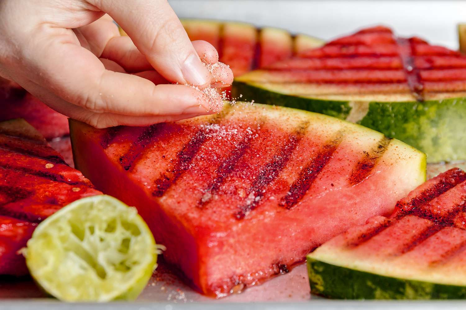 Hand sprinkling spice mix over triangle of grilled watermelon