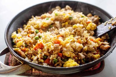 A black skillet with prepared pork fried rice recipe inside. Steam is coming up from the dish and a spatula is resting in the rice on the left side.