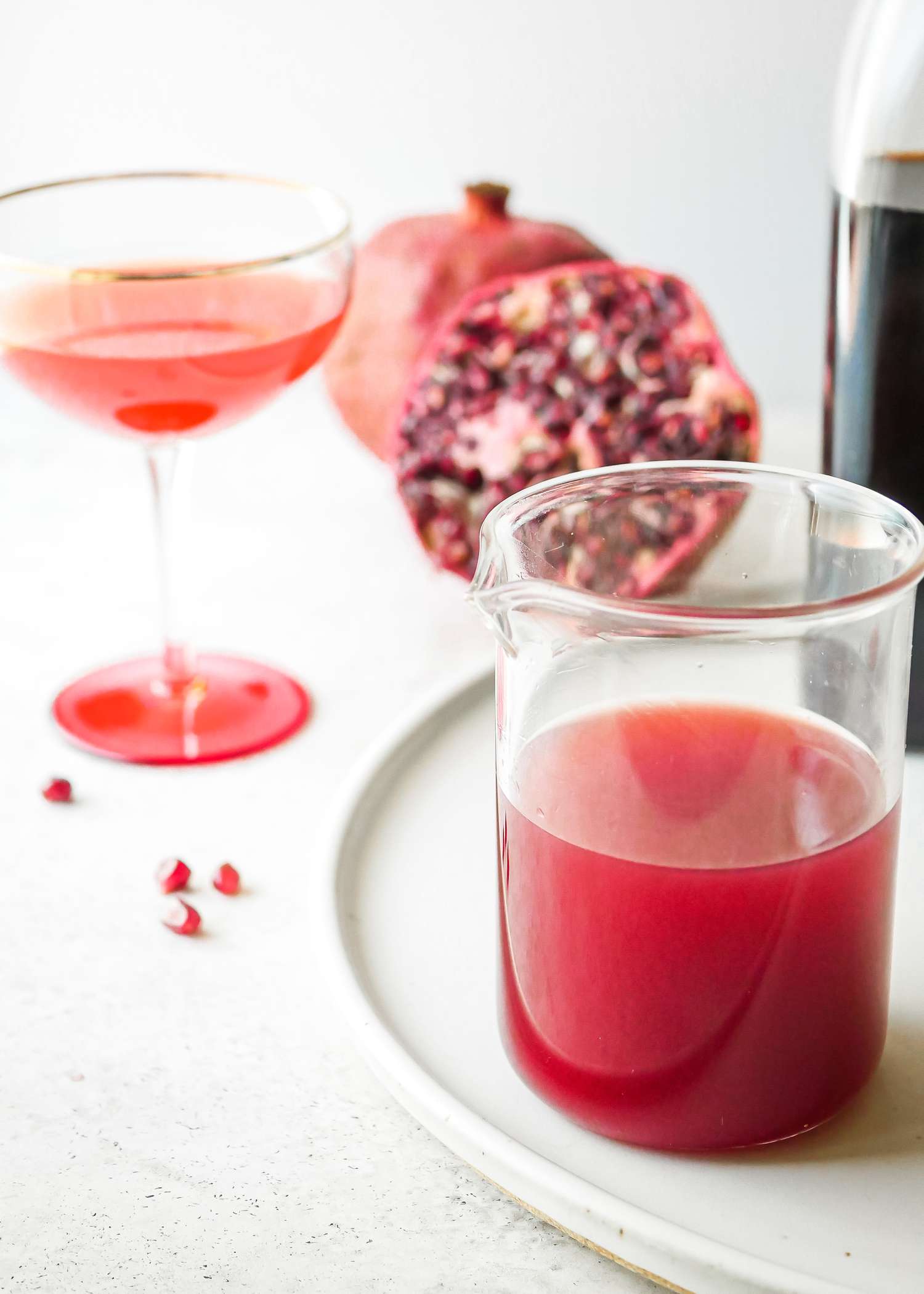 Grenadine Cocktail Syrup in a cocktail mixing glass with halved pomegranate behind it.