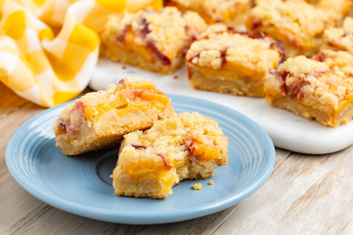 Peach pie bars stacked on a plate, one with a bite out of it