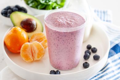 Smoothie in a glass on a platter with some fruit 