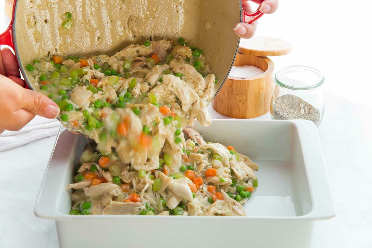 Filling for a favorite chicken pot pie is being poured into a white casserole dish.