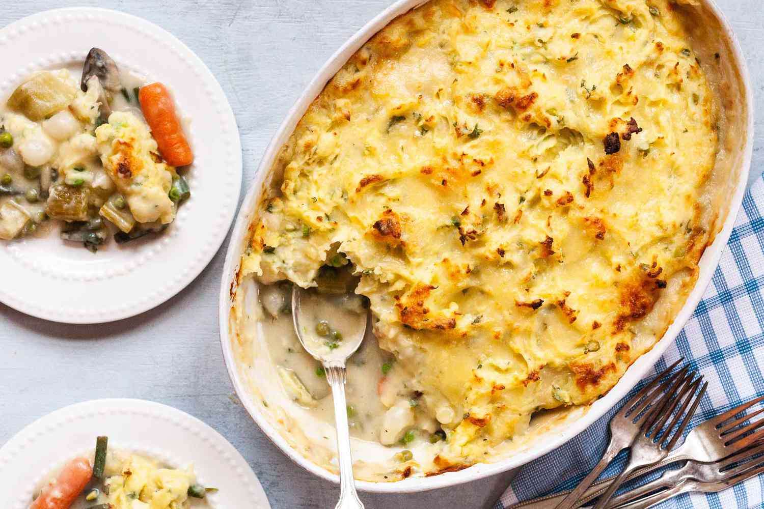 Vegetarian Shepherd’s Pie Recipe -- top down shot of shepards pie scoop taken out, golden and crispy edge mashed potatoes on top. Blue check table cloth, and a plate with some sheperd'e pie serve on top of it.
