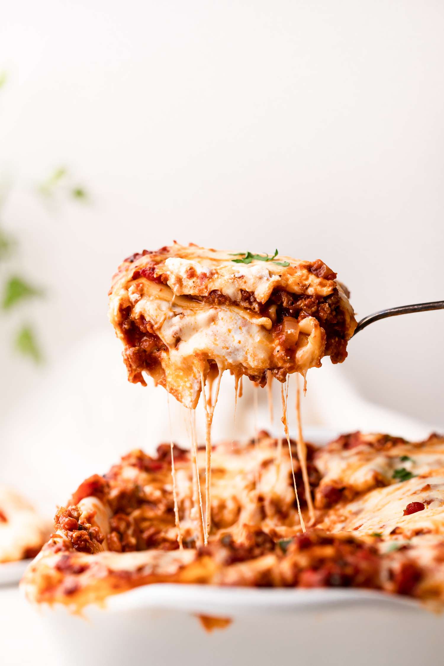 Lifting a piece of lasagna from the pan viewed from the side for a lasagna recipe.