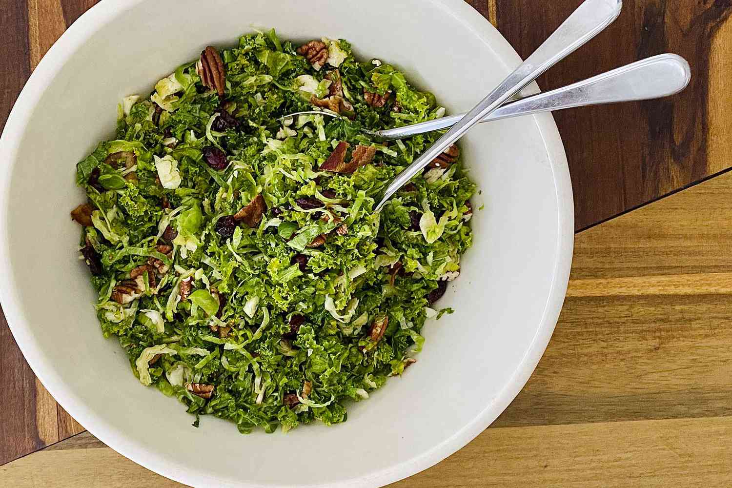 A serving bowl with Raw Kale and Shaved Brussels Sprout Salad with Maple Dijon Vinaigrette ready to be served.