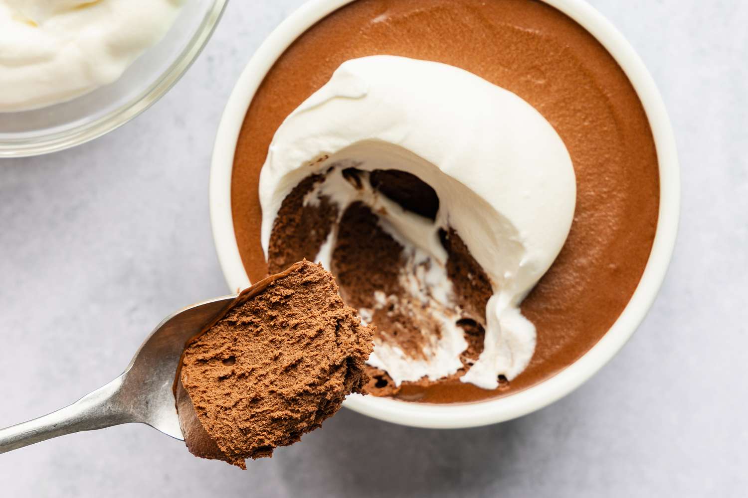 A bowl of mocha mousse topped with whipped cream, with a spoon lifting a portion