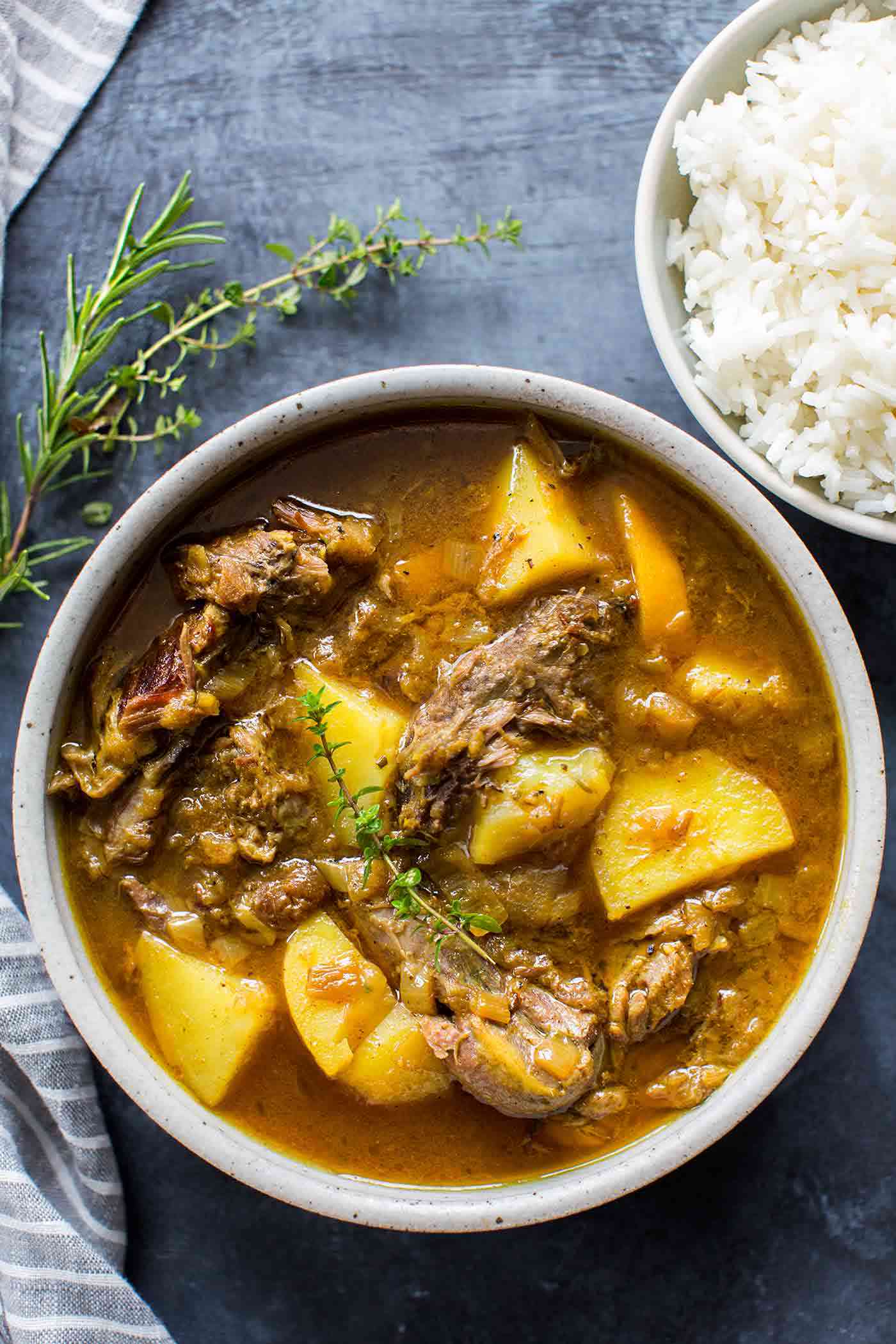 A bowl of lamb curry with rice and herbs on the side