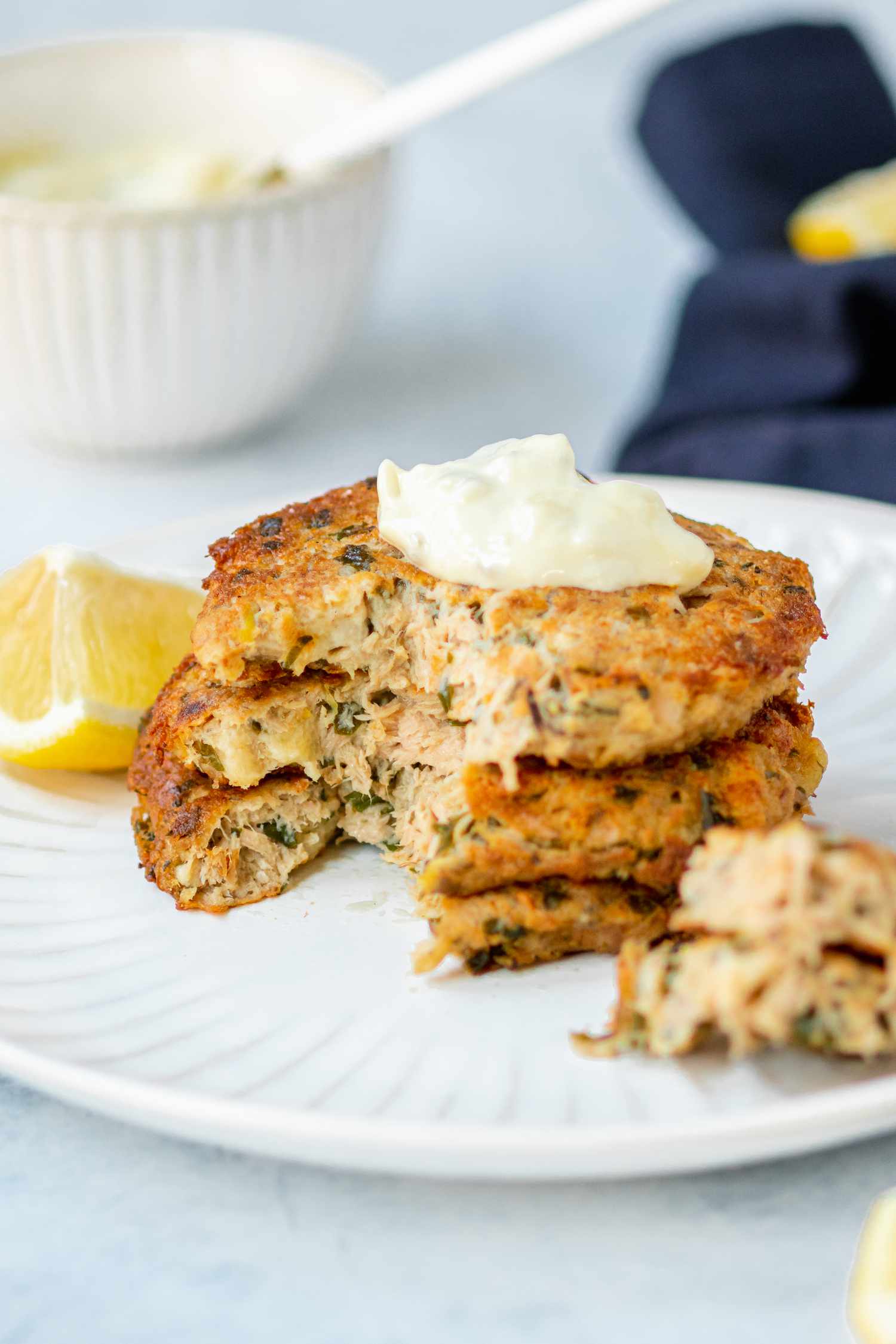 Tuna patties topped with sauce and stacked on a plate with a forkful of patties removed and set next to it.