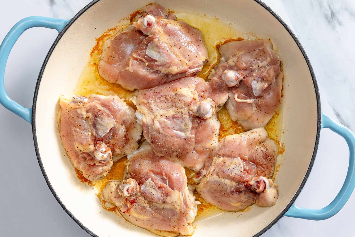 Overhead view of a light blue dutch oven while browning six chicken thighs for Wine Chicken recipe