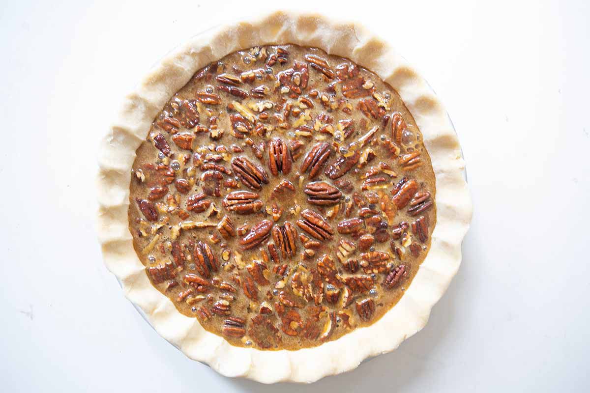 A pecan filling poured over chopped pecans resting in a pie crust 