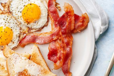 Plate of Microwave Bacon with Sunny Side Eggs and Slices of Buttered Toast