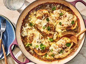 Overhead view of a skillet of Salsa Verde Chicken with a wooden serving spoon next to a plate with fork and knife and a drink glass