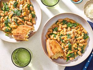 Overhead view of a bowl of 10-Minute Beans and Greens with a chunk of bread all next to a spoon and resting on a blue cloth napkin