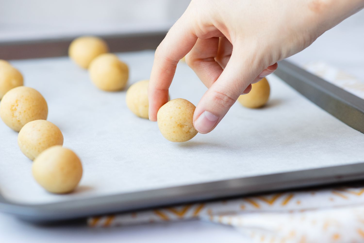 Balls of dough set on a parchment covered baking sheet to make a Chinese almond cookie recipe.