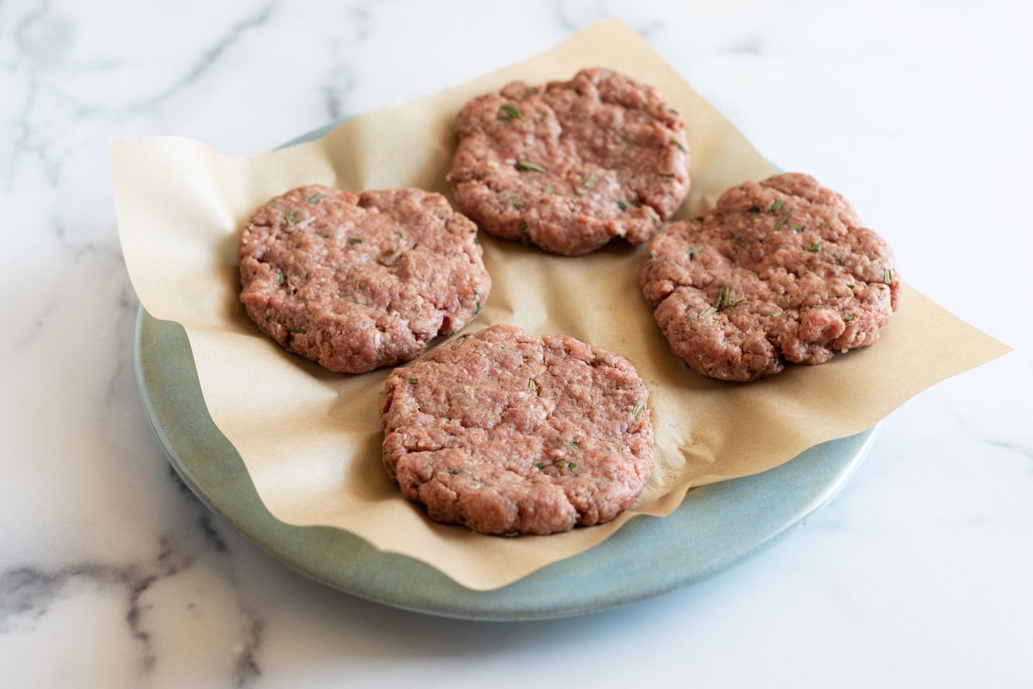 Four burger patties on a plate.