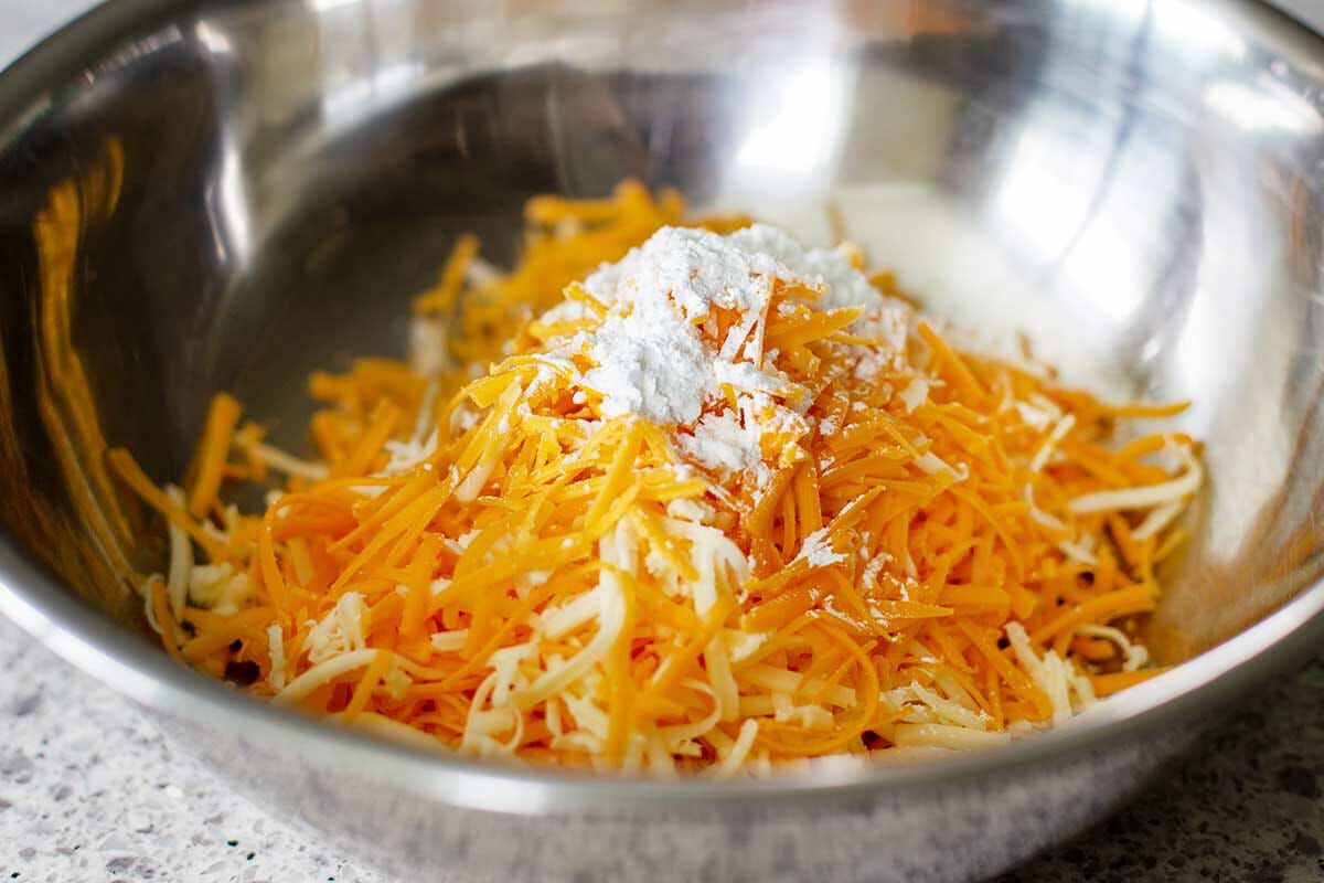A metal mixing bowl has shredded cheese and cornstarch to make Vegetarian Cauliflower Casserole.