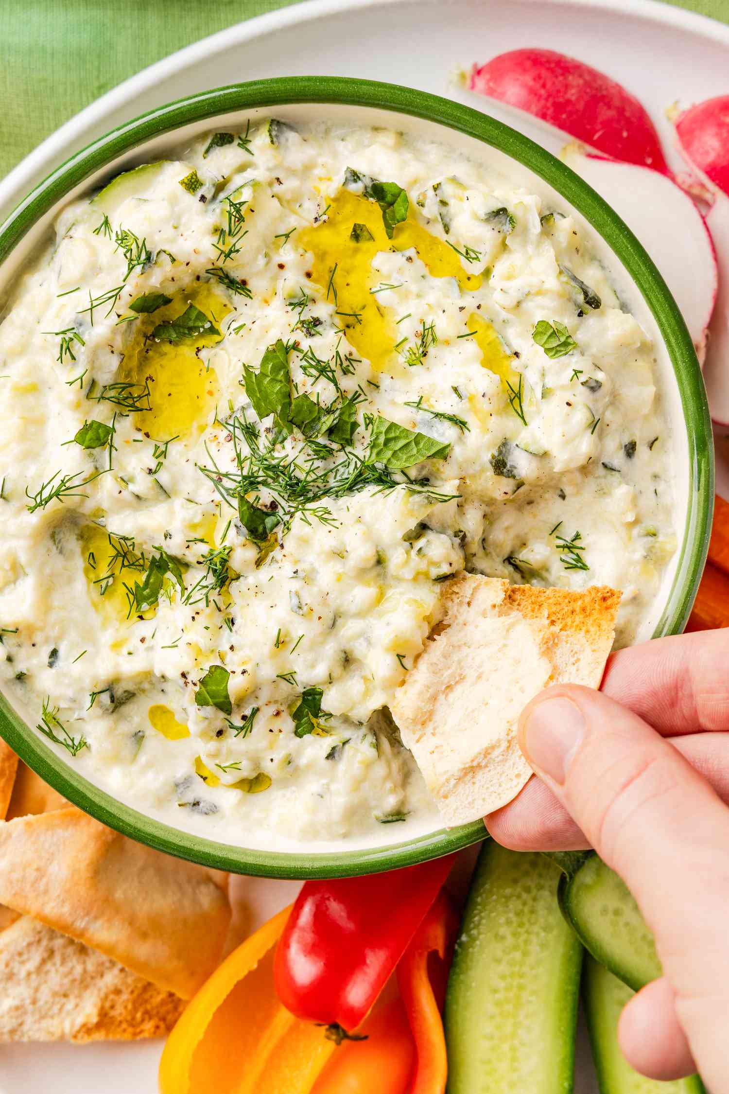 someone dipping a chip in a bowl of zucchini dip on a plate with sliced vegetables