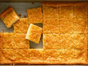 Overhead shot of butter mochi baked in a rectangular baking dish, cut into squares with some pieces taken out