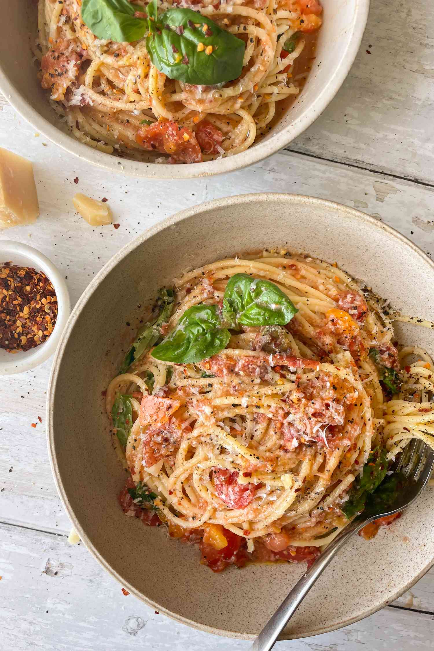Bowl of No Cook Tomato Sauce Pasta Next to a Block of Parmesan Cheese and a Small Dish of Crushed Peppers 