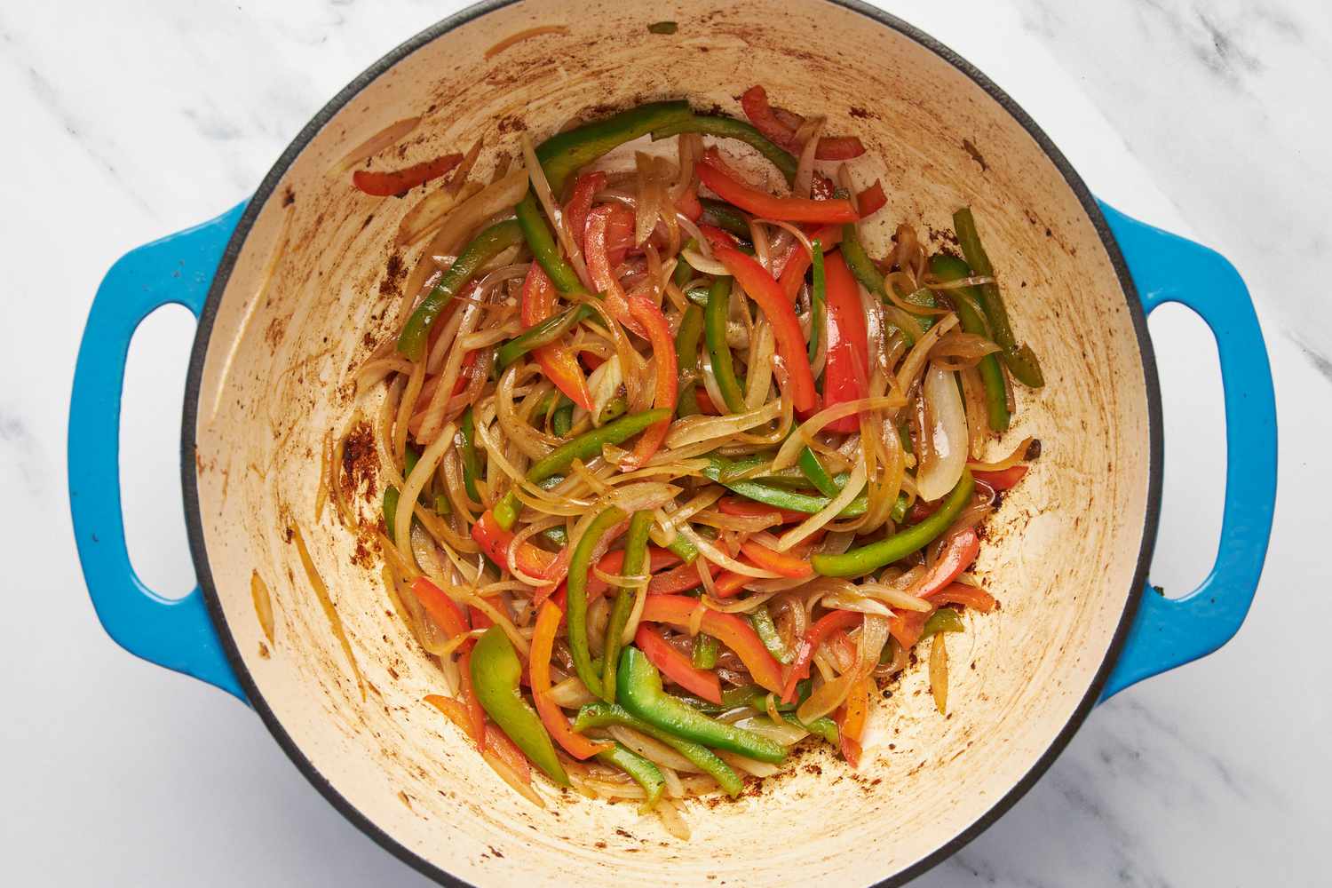 Thinly sliced onions and bell peppers cooked in a Dutch oven for carne picada recipe