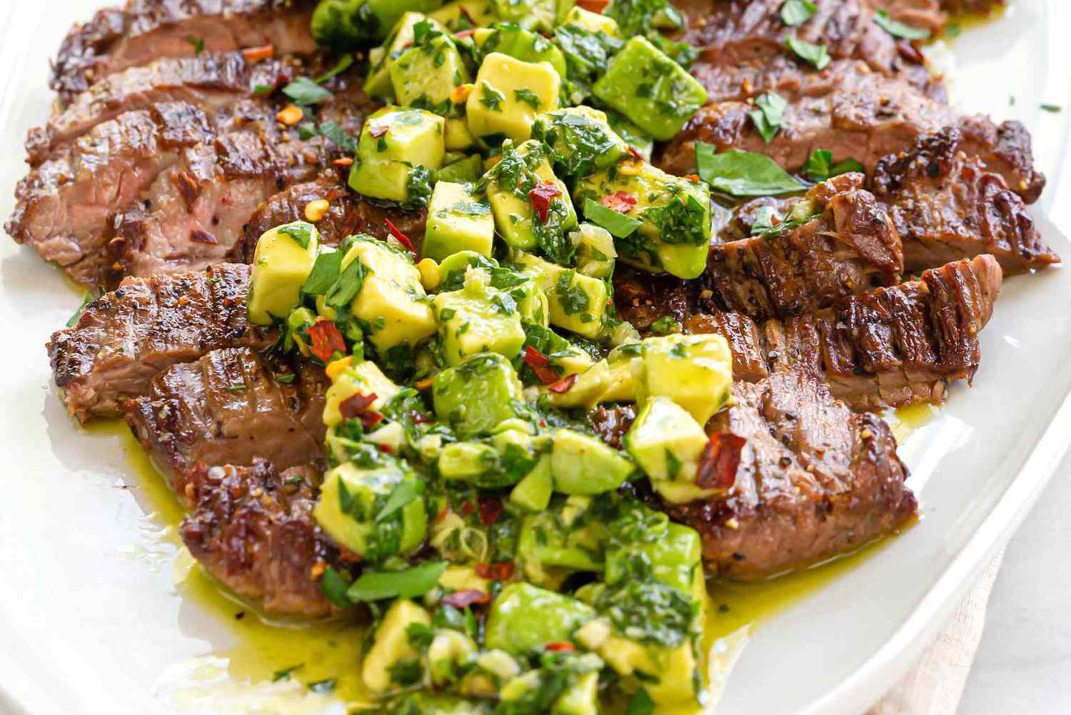 Quick and Easy weeknight skirt steak sliced across the grain and covered with avocado chimichurri on a white plate