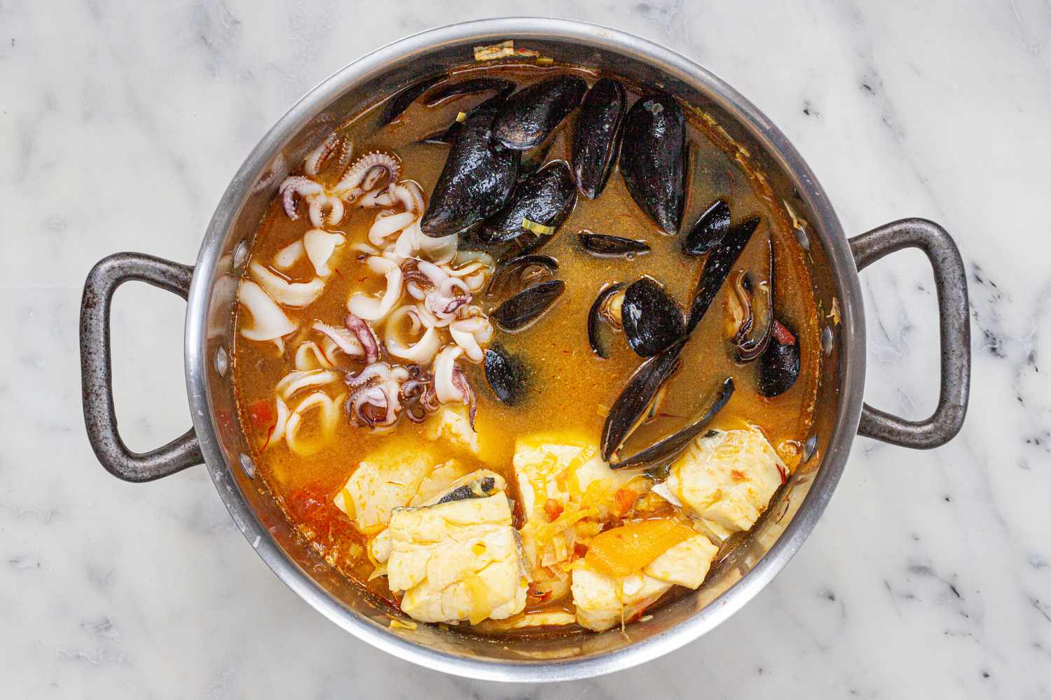 Adding seafood to a stock pot for a bouillabaisse recipe.