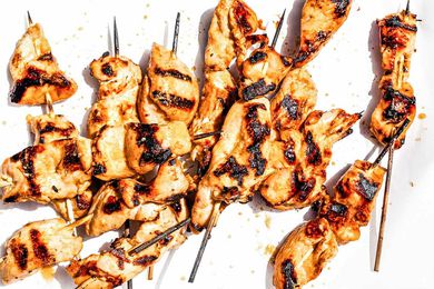 Chicken satay skewers grilled with charred marks, arranged on a white background